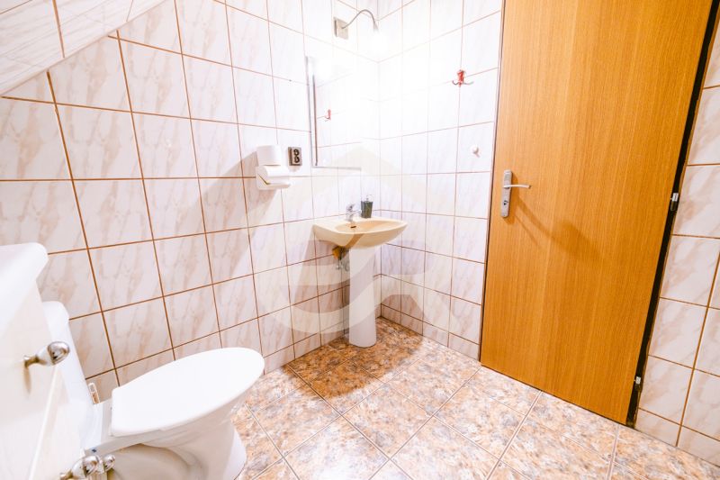 A bathroom in a family house with tiles and a toilet next to the sink.