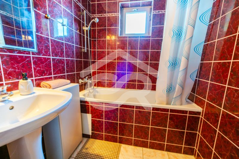 A bathroom in a family house with red tiles, a bathtub, and a sink.