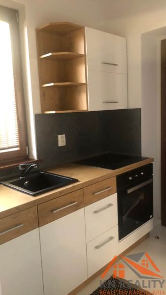 A kitchen unit in a 2-room apartment with a black sink and white cabinets.