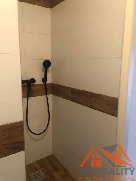 Shower corner with ceramic tiles and a showerhead in a 2-room apartment.