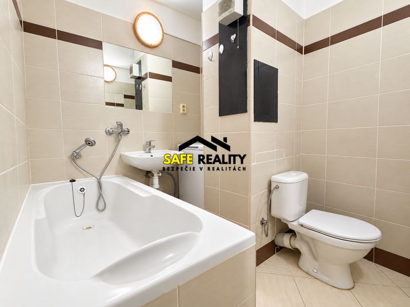 Bathroom in a studio apartment with a bathtub, sink, and toilet, tiled with light tiles.