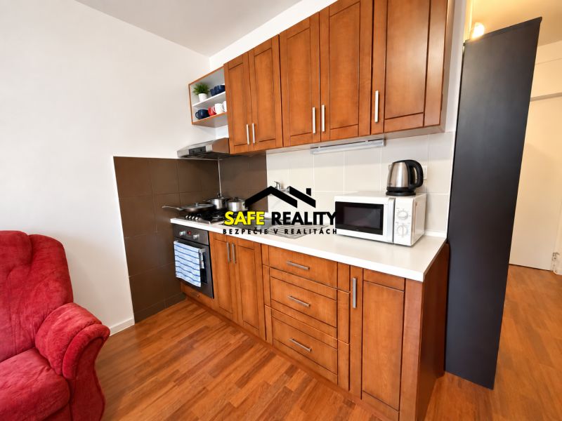 A kitchen in a studio apartment with a wooden decor floor and appliances.