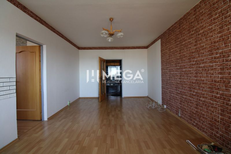 A room in a 3-room apartment with a wooden decor floor and a brick pattern on the wall.