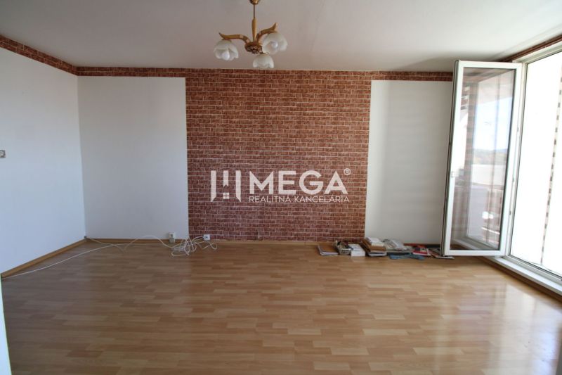 A room with brick cladding, a floor with a wooden decor, and a large window in a 3-room apartment.
