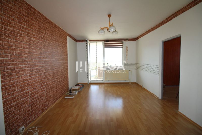 A room in a 3-room apartment with a wooden decor floor and brick wallpaper.