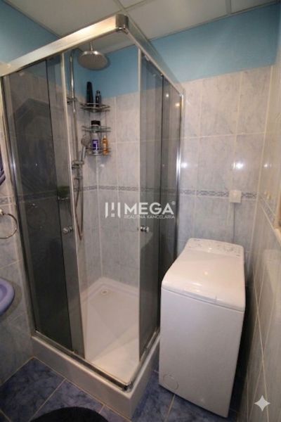 A bathroom in a 3-room apartment with tiles, a shower corner, and a washing machine.