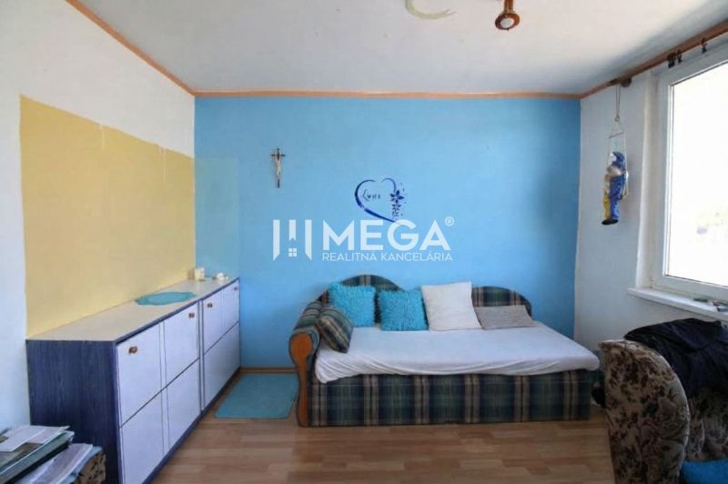 A room with a blue wall, a sofa, and a wardrobe in a three-room apartment with a wooden decor floor.