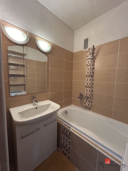 Bathroom with a shower tub in a 2-room apartment, light tiles, washbasin cabinet.