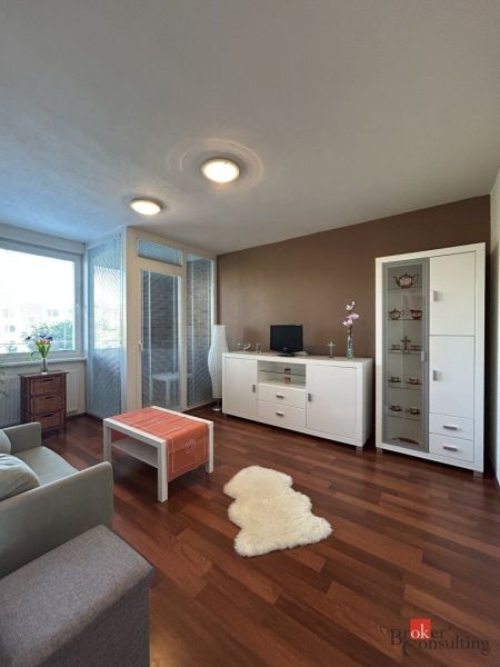 Living room in a two-room apartment with a wooden decor floor, white furniture, and light-colored walls.
