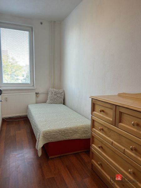 A room in a 2-room apartment with a bed, a dresser, and a floor with a wooden decor.