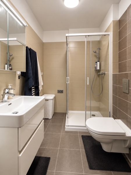 A bathroom in a 2-room apartment with a modern shower, built-in sink, and light tiles.
