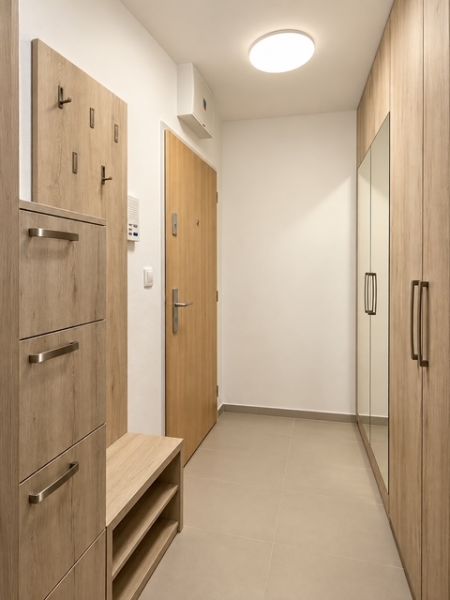 A hallway in a 2-room apartment with built-in wardrobes and a coat rack in light wood decor.
