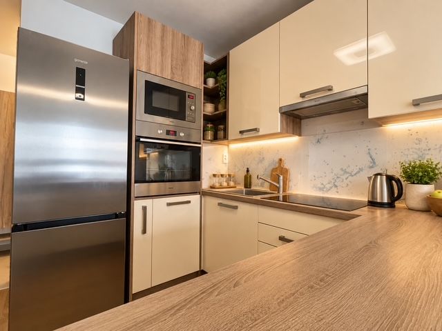 A kitchen in a 2-room apartment with a stainless steel countertop and appliances, and a floor with a wood decor.