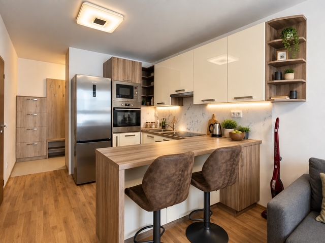 A kitchen in a 2-room apartment with appliances and a wooden decor floor.