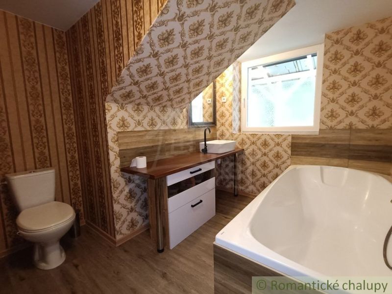 A bathroom in a family house with wallpaper and a wooden decor floor.