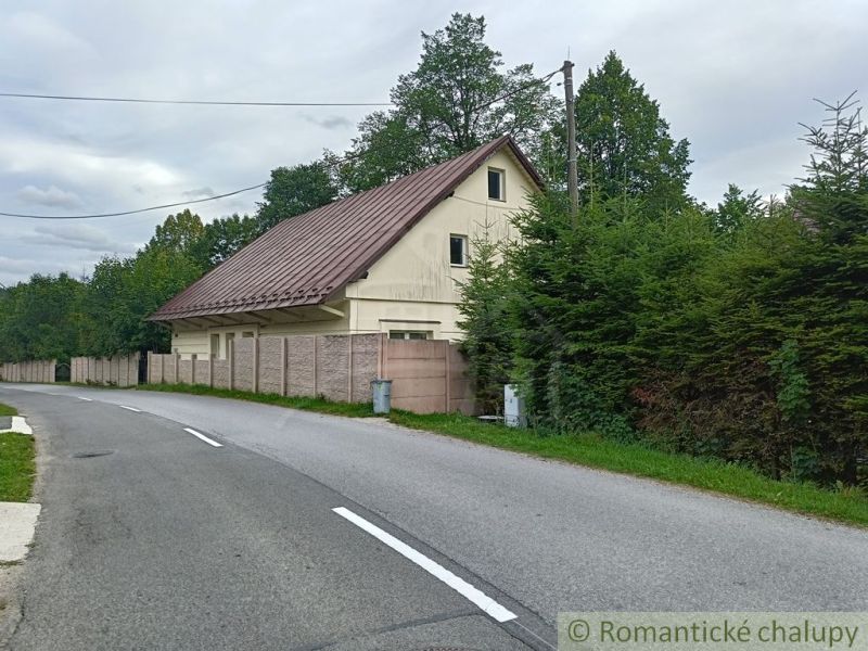 A family house in Staškov with a metal roof, surrounded by trees and a fence.