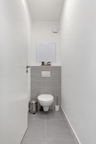 A narrow toilet with white walls and gray tiles in a two-room apartment.