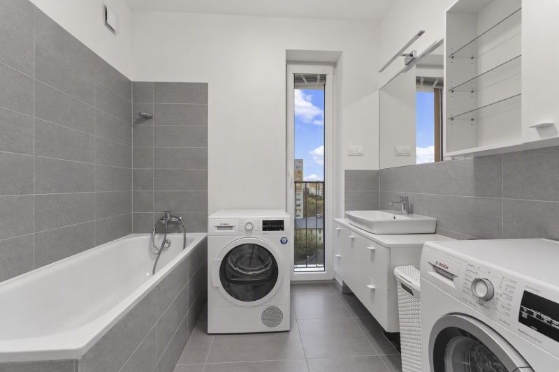 Bathroom with a bathtub, washing machines, and a sink in a 2-room apartment. Gray tiles, large mirror.