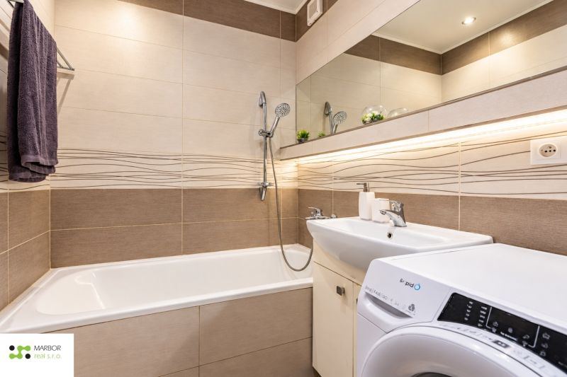 Bathroom with a bathtub and a sink in a 3-room apartment with a mirror and a washing machine.