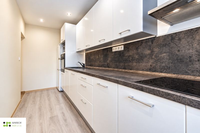 A kitchen in a 3-room apartment with white furniture and a wooden decor floor.