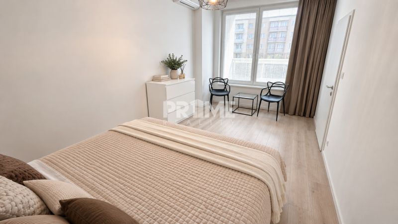A bright bedroom in a two-room apartment with a wood-patterned floor and simple furniture.