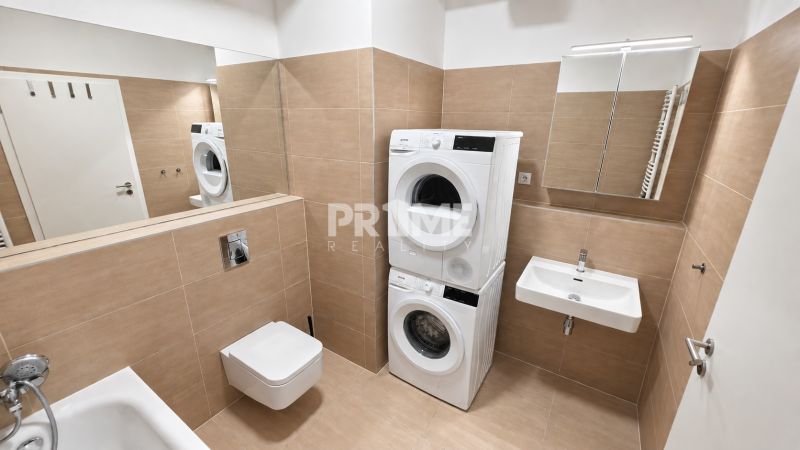 Bathroom of a two-room apartment with a shower, sink, toilet, and a washer with a dryer.