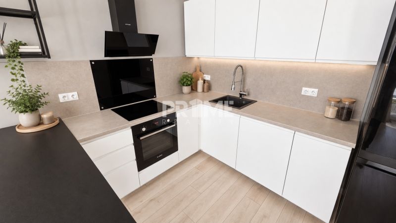 A kitchen in a 2-room apartment with white cabinets, a cooktop, and a wooden decor floor.