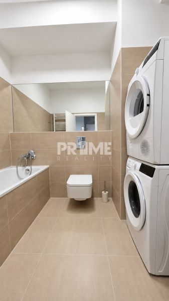 Bathroom of a 2-room apartment with a shower, washing machine, dryer, and beige tiles.