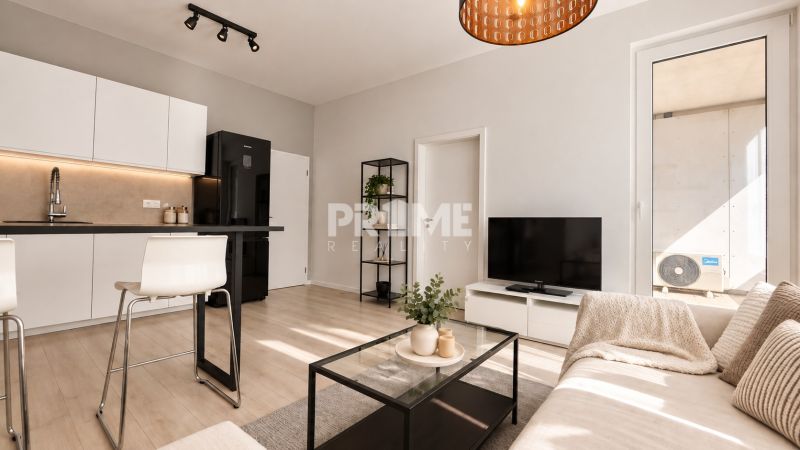 A bright living room in a two-room apartment with wood-patterned flooring, white cabinets, and a sofa.