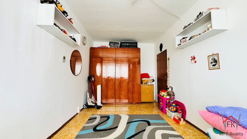 A room in a 3-room apartment with a carpet, toys, and a cabinet with a wood decor.