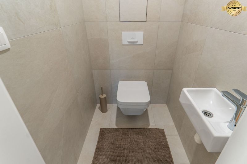 Toilet with a wall-hung toilet, small sink, and beige tiles, Apartment construction.
