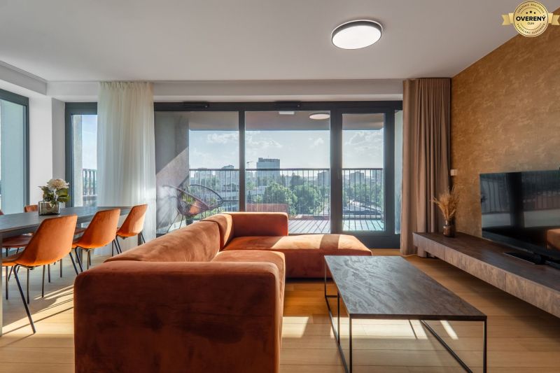 Living room with an orange sofa, dining table, and a view of the city. Apartment construction.