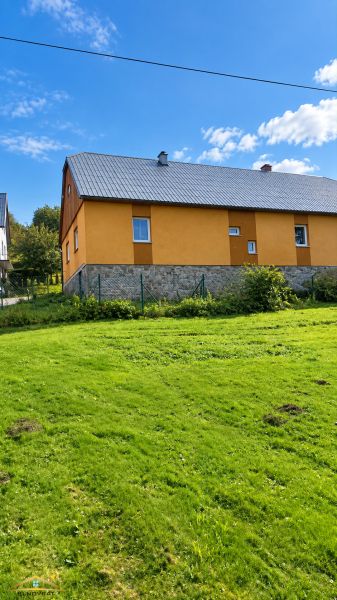 A family house in Oščadnica on Košariská Street with a yellow facade and a grass-covered plot.