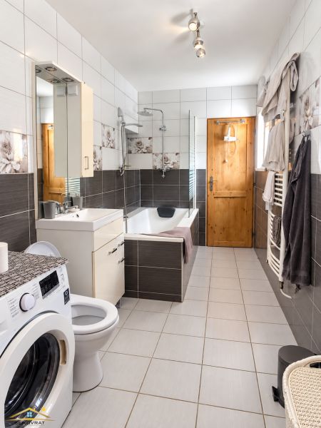 A bathroom in a family house with a washing machine, a bathtub, and tiles in neutral colors.