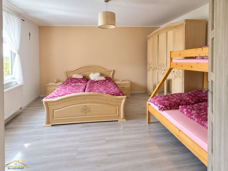 A bedroom in a family house with a large bed, a bunk bed, and a floor with a wooden decor.