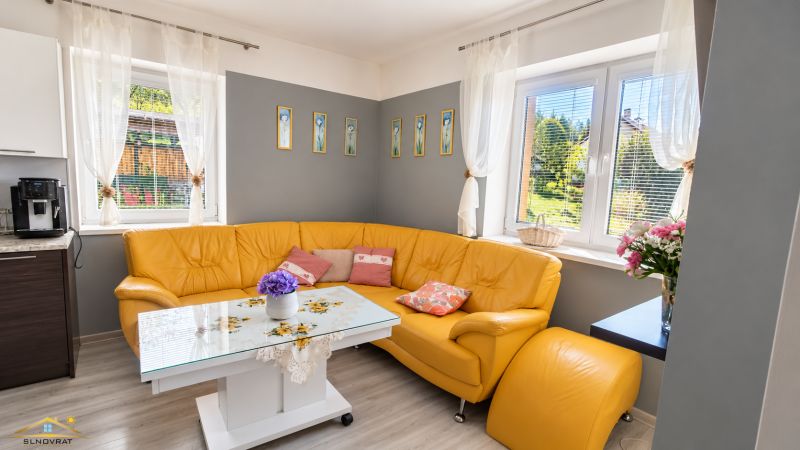 Corner sofa in the living room of a family house with floral decoration and wooden decor flooring.