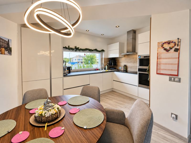A kitchen in a family house with a dark table, modern lighting, and a floor with a wooden decor.