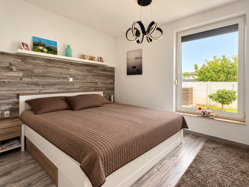 A bedroom with a brown bed, wooden paneling, and a wooden decor floor in a family house.