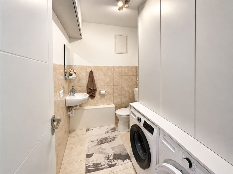 A bathroom in a family house with a washing machine, dryer, and beige tiles.