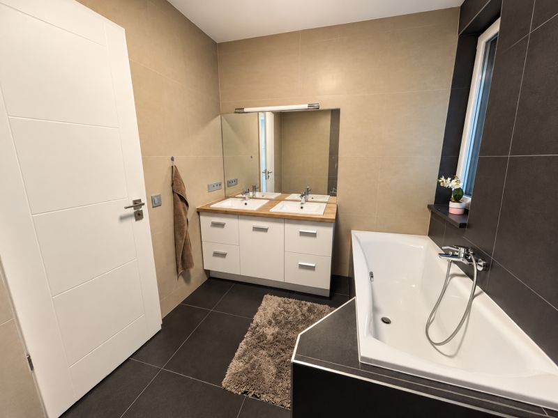 Bathroom in a family house with a bathtub, mirror, and cabinet under wooden decor.