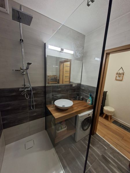 Bathroom with a sink, shower, and washing machine in a studio apartment, floor with wooden decor.