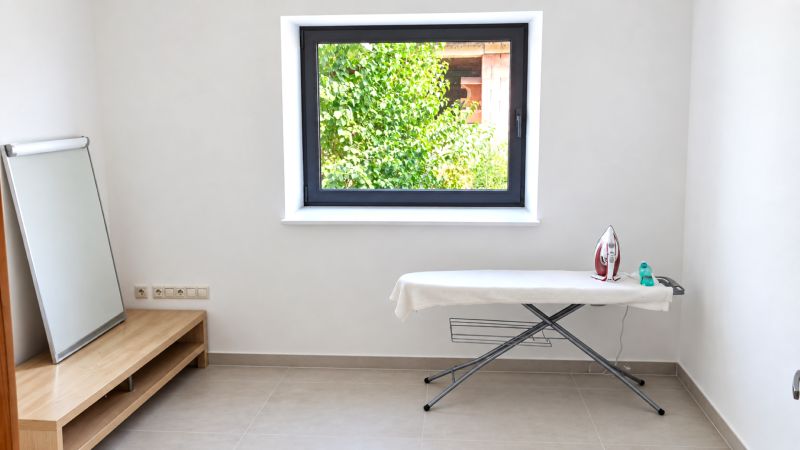 Ironing board with an iron in a room with a window and a mirror in a family house.