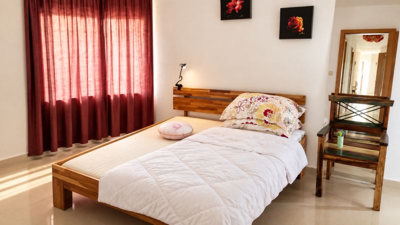 Bright bedroom with a bed, mirror, and red curtains in a family house.