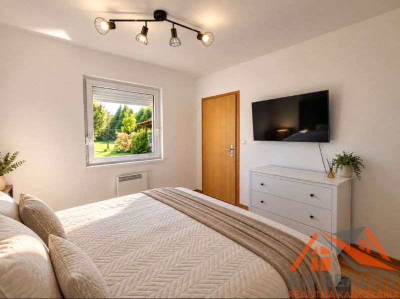 A bedroom in a family house with light furniture, a window, and a TV on the wall.