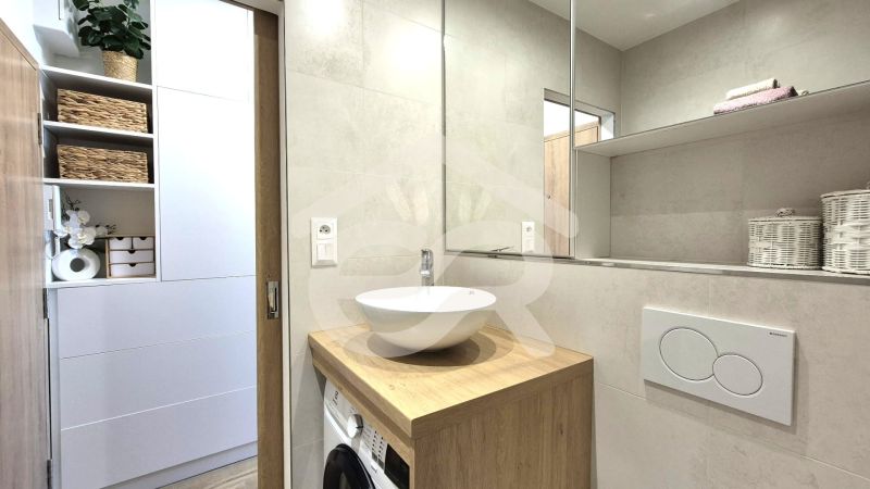 A bathroom in a studio apartment with a white sink, wooden decor, and storage baskets.