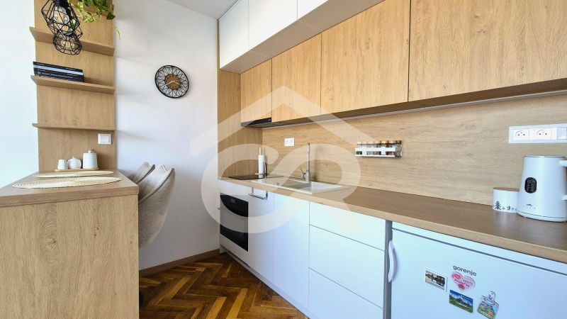 A kitchenette in a studio apartment with a wood-patterned floor and built-in appliances.