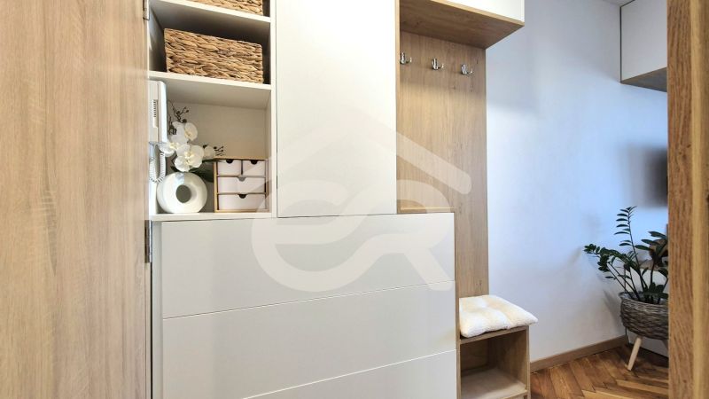 A studio apartment interior with wooden furniture, decorations, and a plant on a wooden-patterned floor.