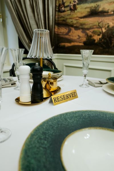 A reserved table with place settings in a business establishment, includes spice shakers and elegant glasses.