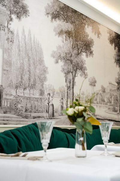A wall with a historical painting, a table with flowers and glasses in a commercial space.