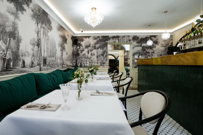 Interior with historical wallpaper, tables, green sofas, and a crystal chandelier in commercial premises.